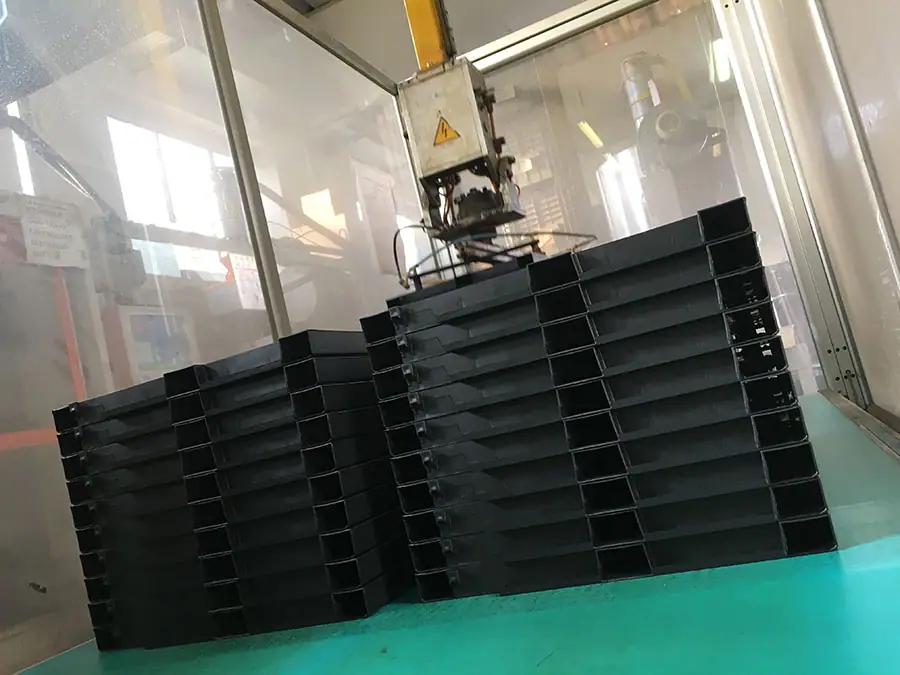 Braccio robotico all’interno di una pressa per stampaggio a iniezione mentre impila componenti plastici industriali neri